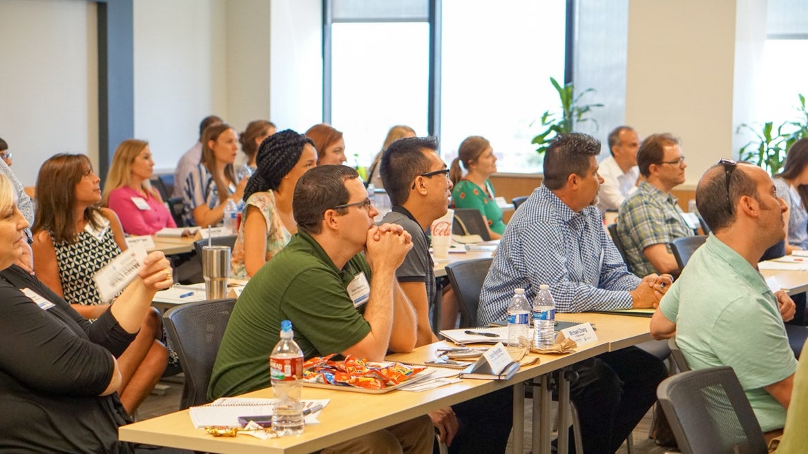 American Express Leaderhip Academy participants sit at tables while listening to a lecture.