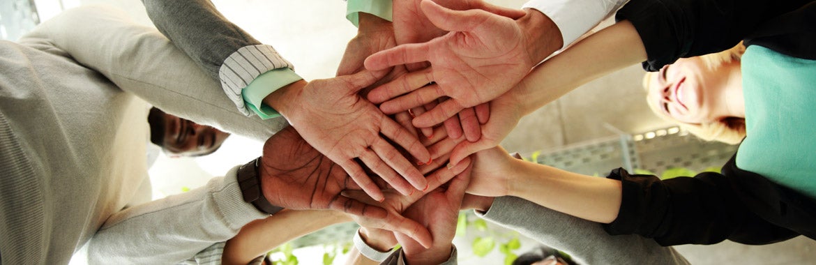 Several people standing in a circle stack their hands on top of the others' hands.