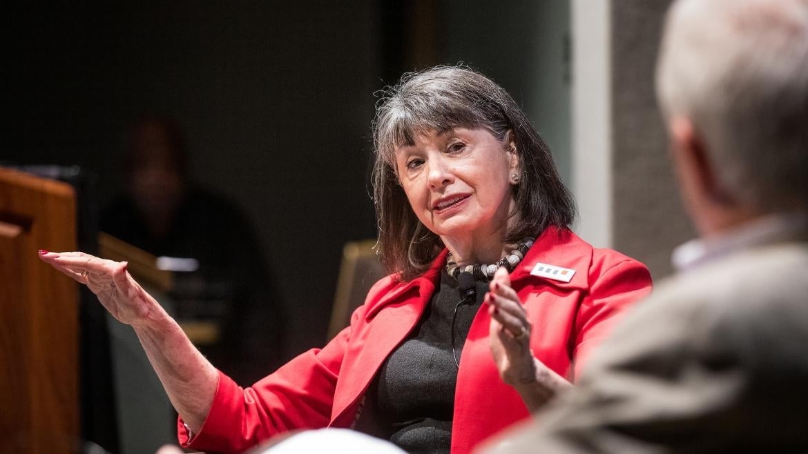 Gloria Feldt sits in a chair and gestures with her hands while speaking.