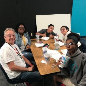 Several people sit around a table while enjoying take-out food.