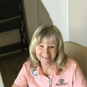 A woman wearing a pink collared t-shirt looks up at the camera and smiles.