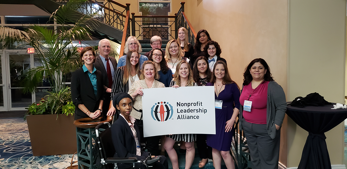 Standing in front of a staircase, students pursuing the Certified Nonprofit Professional Credential gather to hold a sign reading "Nonprofit Leadership Alliance" alongside ASU faculty.