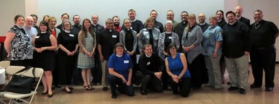 Graduates and faculty of a six-part training for priests in nonprofit management stand together while inside.