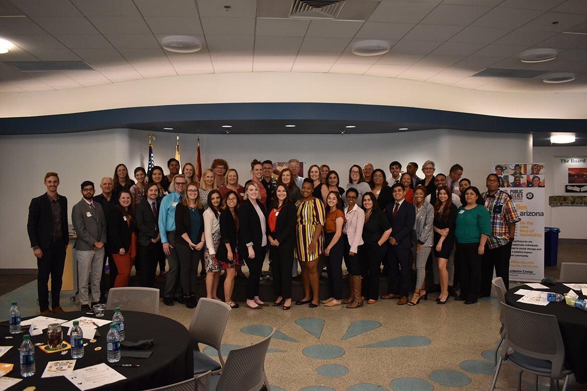 Beside a banner, the attendees of the  2019 Public Allies Arizona Induction Ceremony smile.