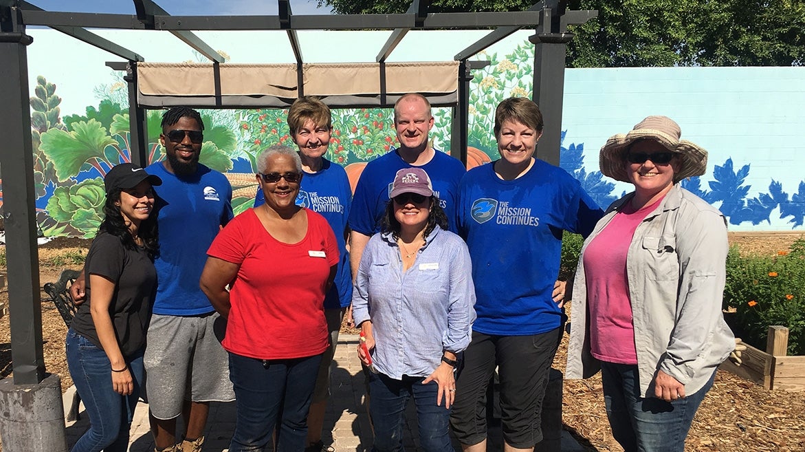 House of Refuge members smile while outside in a garden. Behind them are walls with paintings of plants.