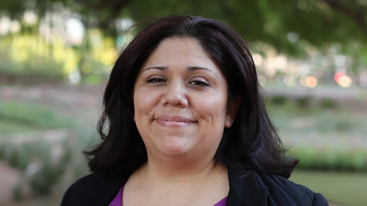 Magdelena Saucedo smiles while outside. Behind her is a garden.