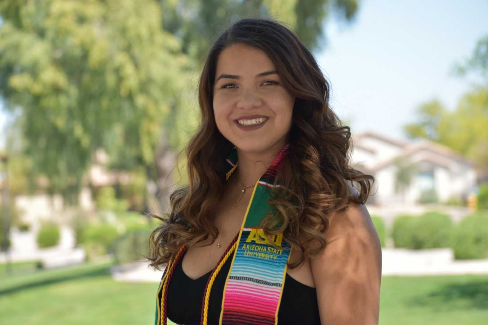 Maricela Diaz smiles while wearing graduation tassles. In the baground is a house.