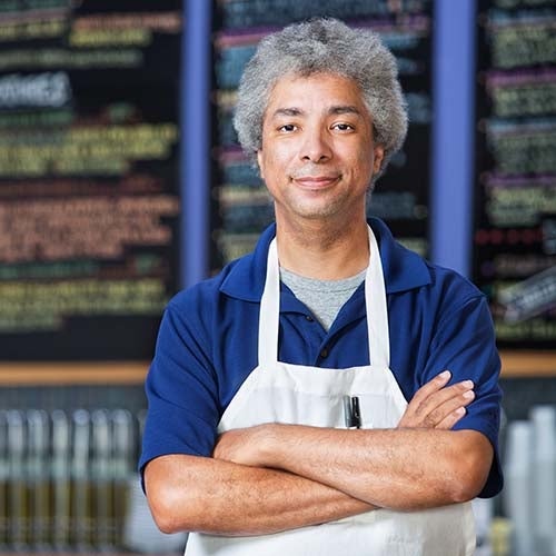 Photo of Mike Edmonds. Edmonds is standing with crossed arms and wearing a white apron.