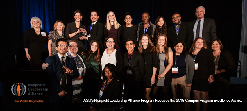 In front of a large dark blue curtain, Nonprofit Alliance Leadership members gather for a photo.