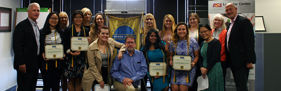 Within an office space, in front of several banners and posters, several initiated Nu Lambda Mu members gather with ASU faculty.