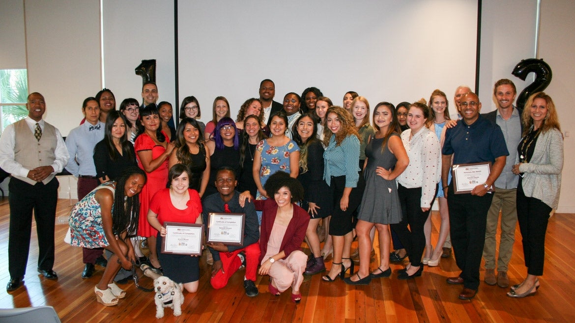 Public Allies Arizona Class 12 graduates gather inside a large auditorium. Some are holding framed certificates.