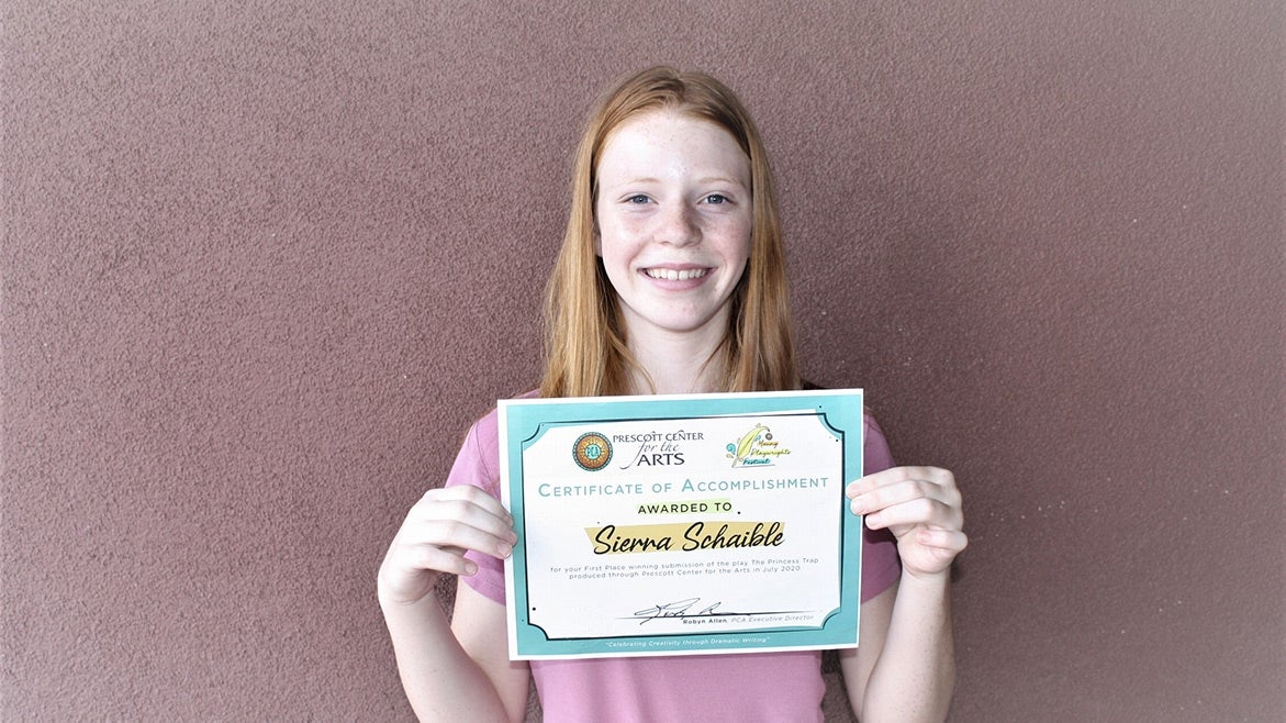 A young person smiles while holding up a paper certificate.