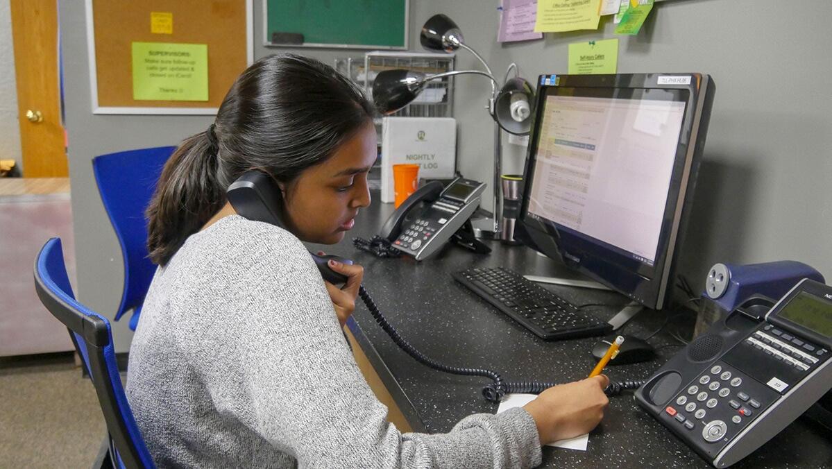 A young person takes a call while sitting at a desk with a computer.